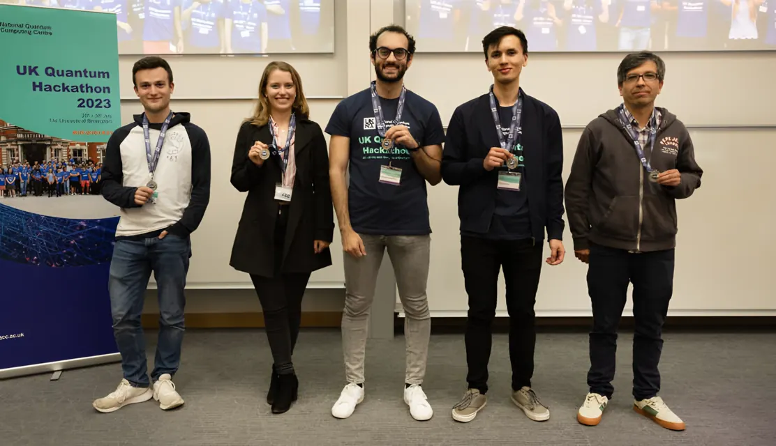 Five team members with medals in front of a UK Quantum Hackathon 2023 banner